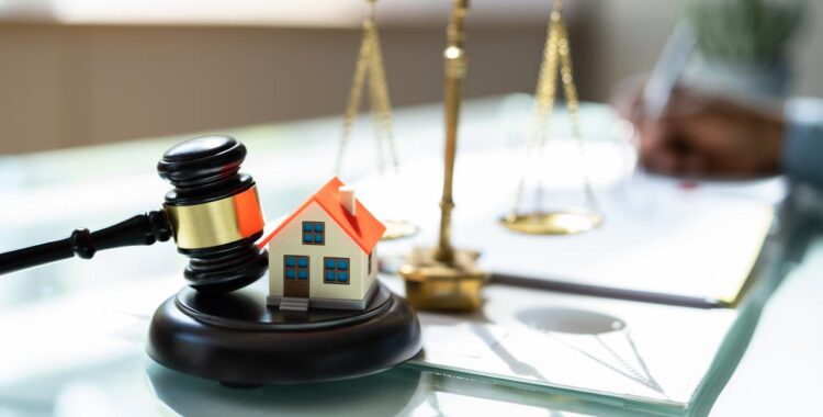 A real estate lawyer's desk with a set of scales, a judge's gavel and block, and a small model of a house.
