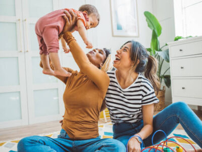 Gay couple with baby at home Young mothers playing with baby girl in living room